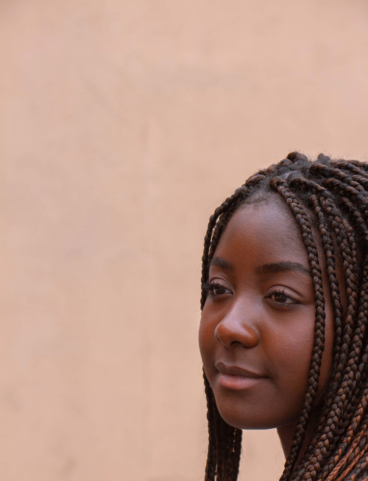A woman with braids against a warm pink background