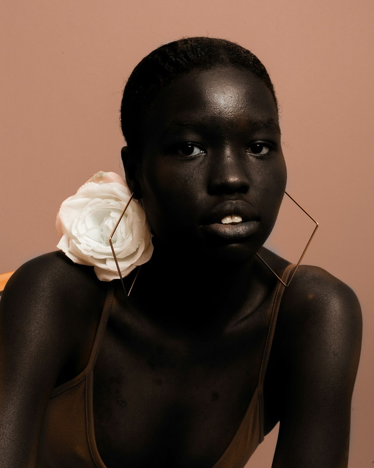 A woman with short hair and a white flower against a warm rose background